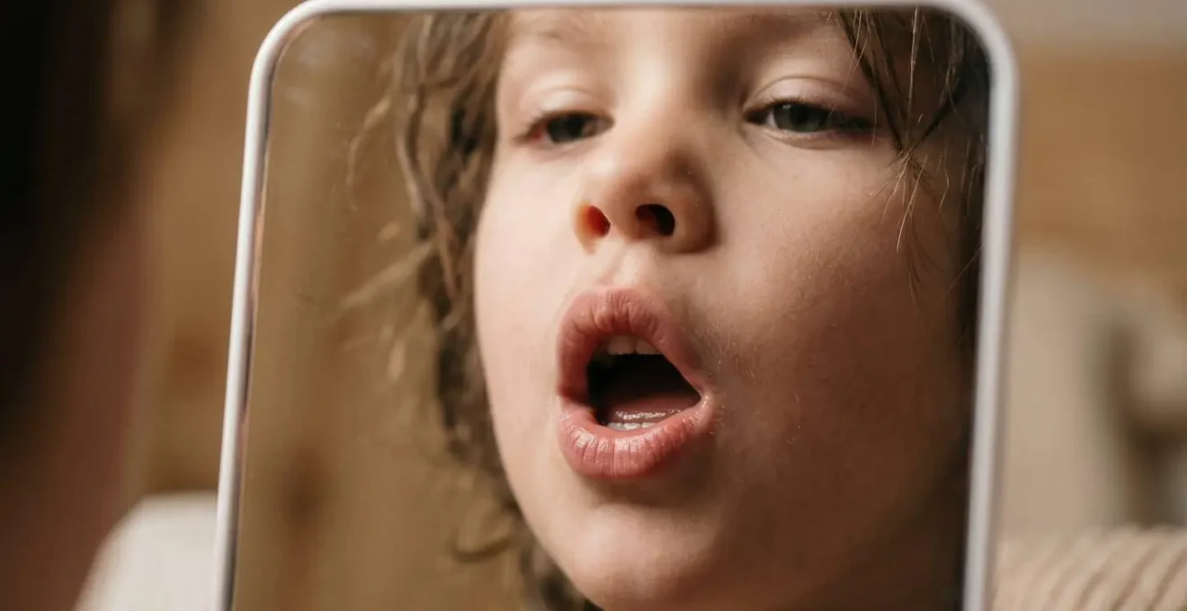 Young child making exaggerated mouth movements in front of a mirror during speech practice