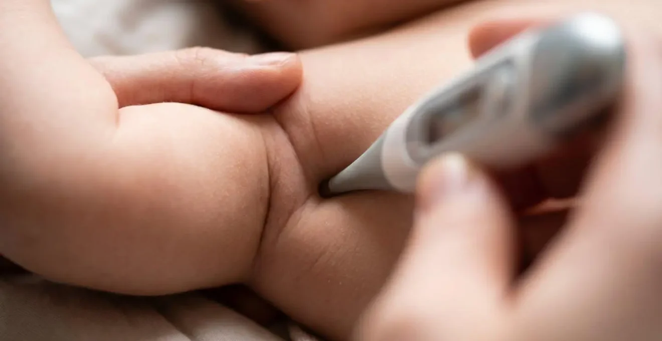 Close-up of digital thermometer measuring infant temperature with parent's gentle hand visible